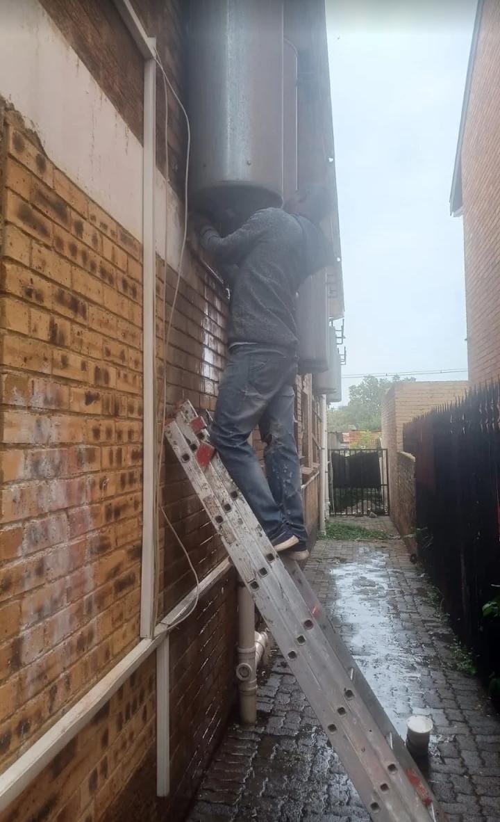 Technician on a ladder servicing a geyser and exterior wall