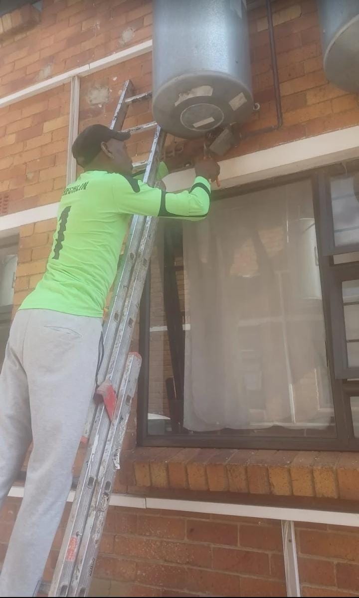 Maintenance work on a geyser from a ladder against a brick wall